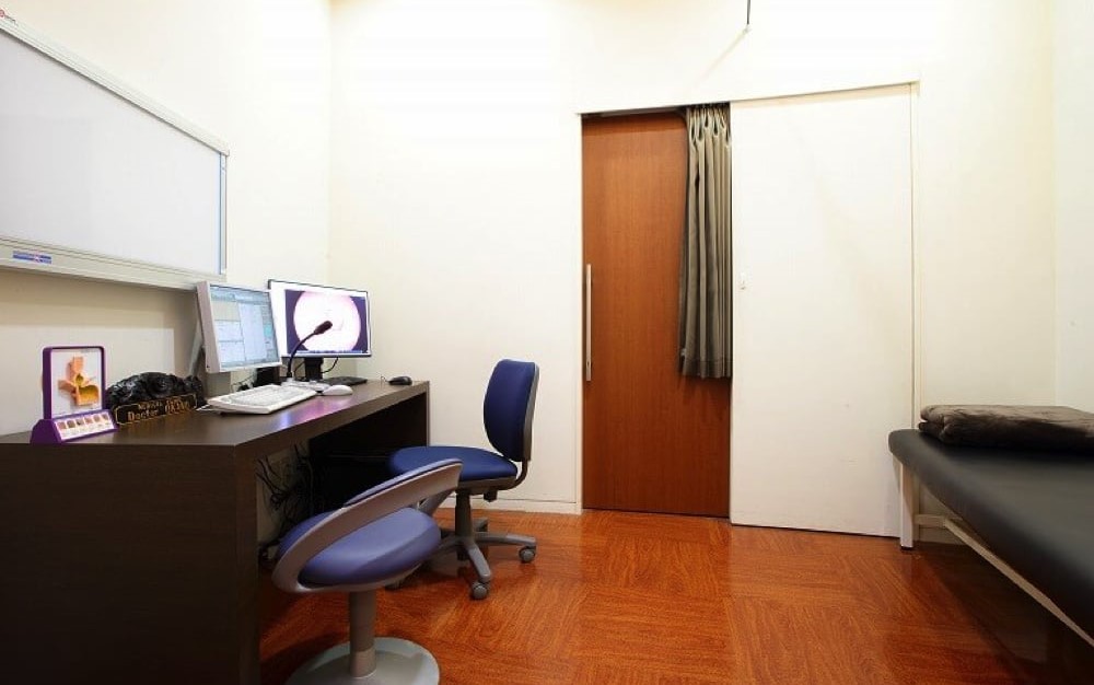 白と茶色を基調とし、椅子と机とベットがあるジュノビューティークリニック渋谷院の診察室